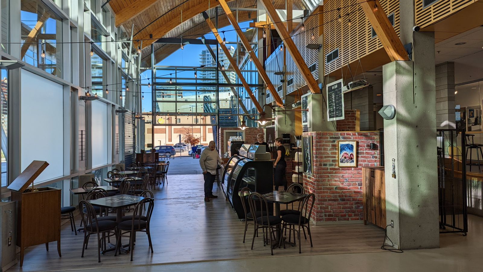 A view of Roma Nord Bistro at the Rotary Centre for the Arts. Sunlight shines on a large open-air bistro through tall windows as workers prepare the bistro for customers